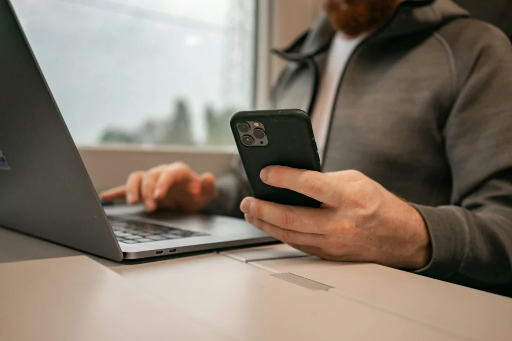 Ein Saloninhaber verwaltet Online-Buchungen auf seinem Smartphone und arbeitet gleichzeitig am Laptop