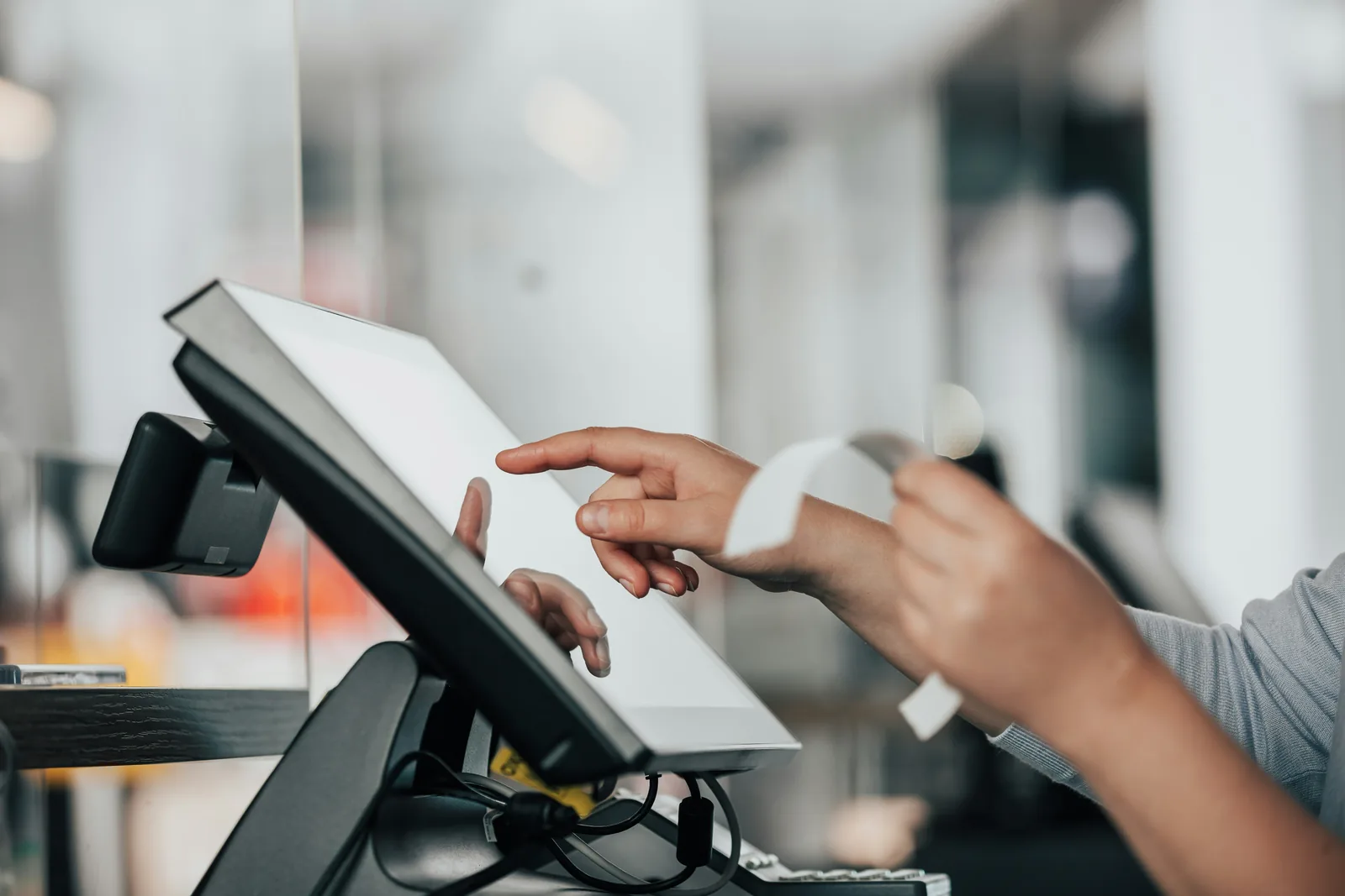 Hände bedienen ein Kassensystem mit Touchscreen an der Theke und reißen einen gedruckten Beleg ab