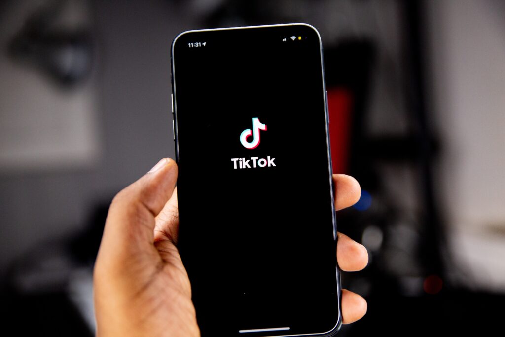 Jemand hält ein Smartphone, dessen Bildschirm das TikTok Logo abbildet.