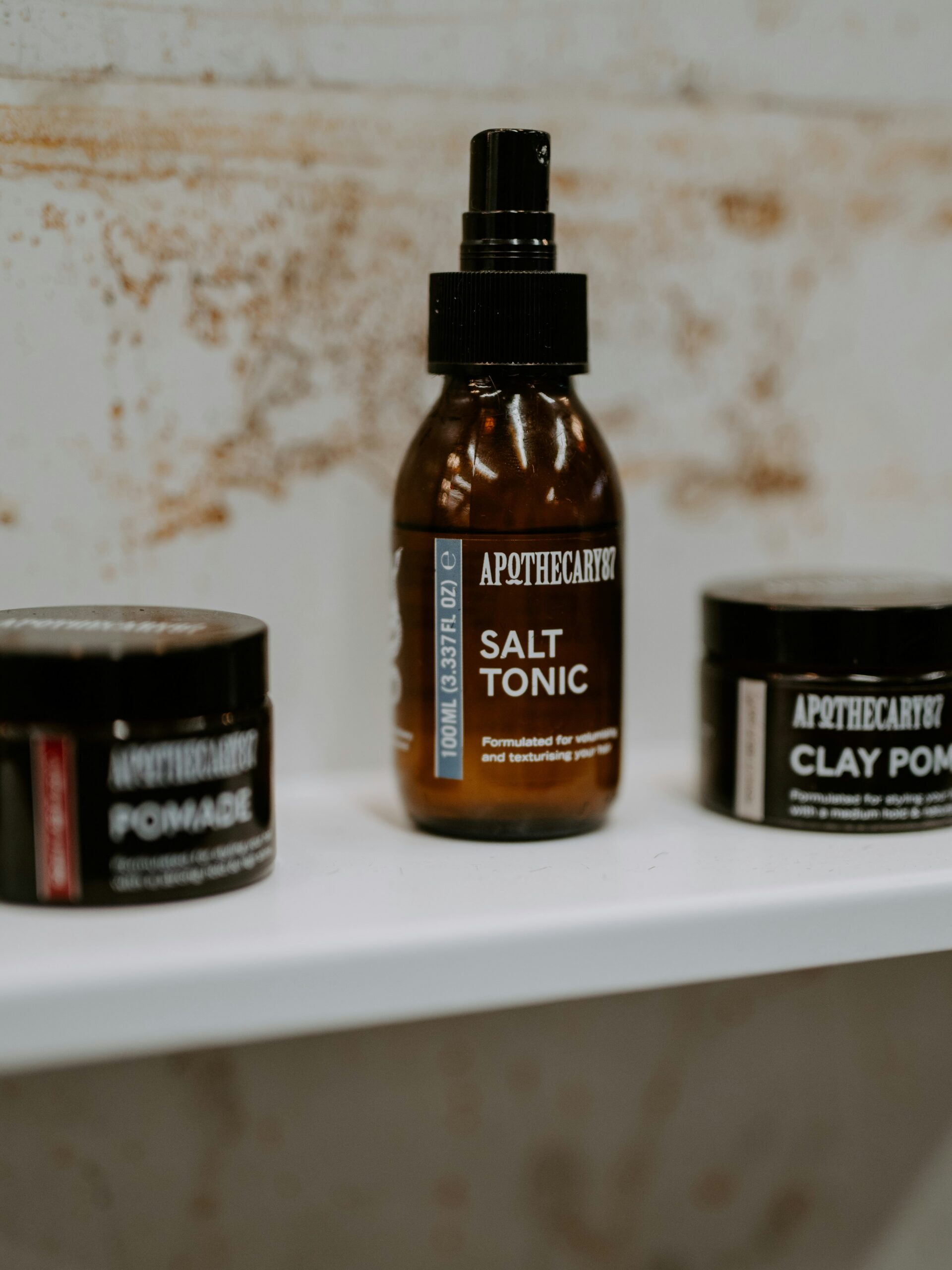 Verschiedene Haarstylingprodukte für Vokuhila-Frisuren in braunen Behltern auf einem weien Regal.