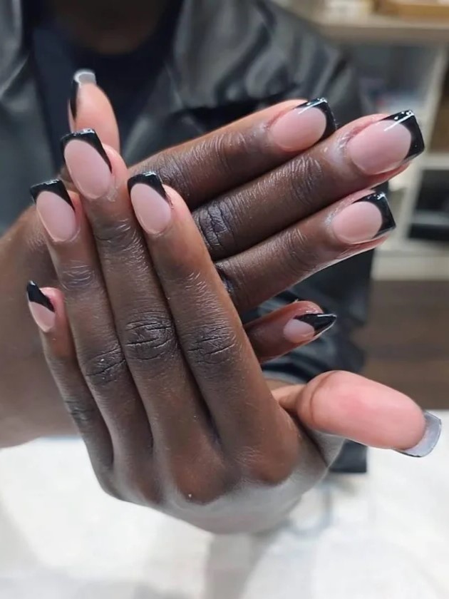 Frau im Nagelstudio zeigt ihre nude BIAB-Maniküre mit schwarzen Verlngerungen in die Kamera
