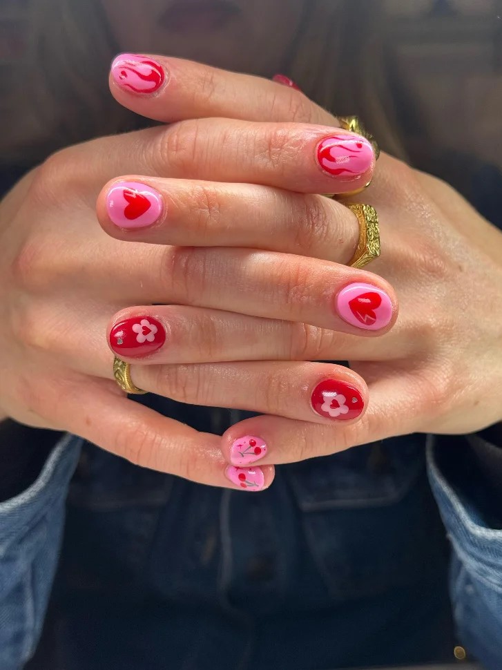 Zusammengelegte Hnde einer Frau mit leuchtend pinker und roter BIAB-Maniküre mit Nail Art