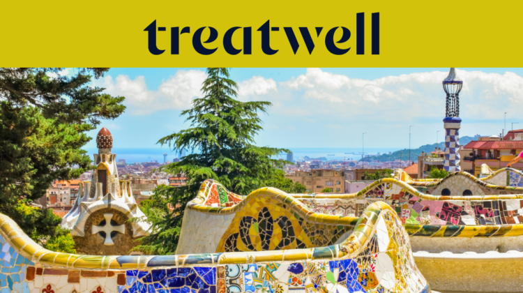 Ein malerischer Blick auf Barcelona vom Park Güell aus, mit Antoni Gaudís berühmten bunten Mosaikbnken und mrchenhaften Türmen im Vordergrund, dahinter die Stadt und das Meer. Ein gelbes Banner am oberen Rand zeigt das "treatwell"-Logo.