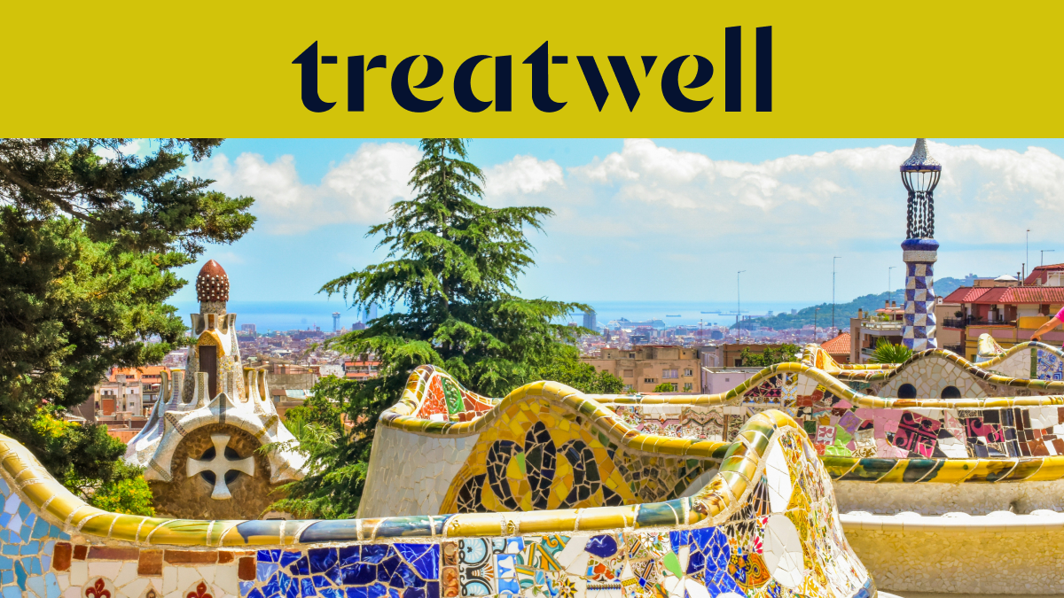 Ein malerischer Blick auf Barcelona vom Park Güell aus, mit Antoni Gaudís berühmten bunten Mosaikbnken und mrchenhaften Türmen im Vordergrund, dahinter die Stadt und das Meer. Ein gelbes Banner am oberen Rand zeigt das "treatwell"-Logo.