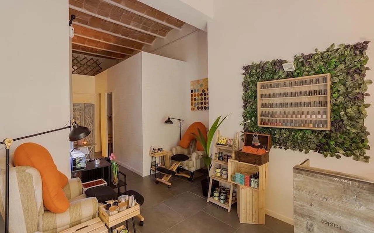Ein gemütliches Nagelstudio im Bohème-Stil mit weichen Sesseln und orangefarbenen Kissen. An der Wand eine groe vertikale Pflanzeninstallation rund um ein Holzregal voller Nagellackflaschen.