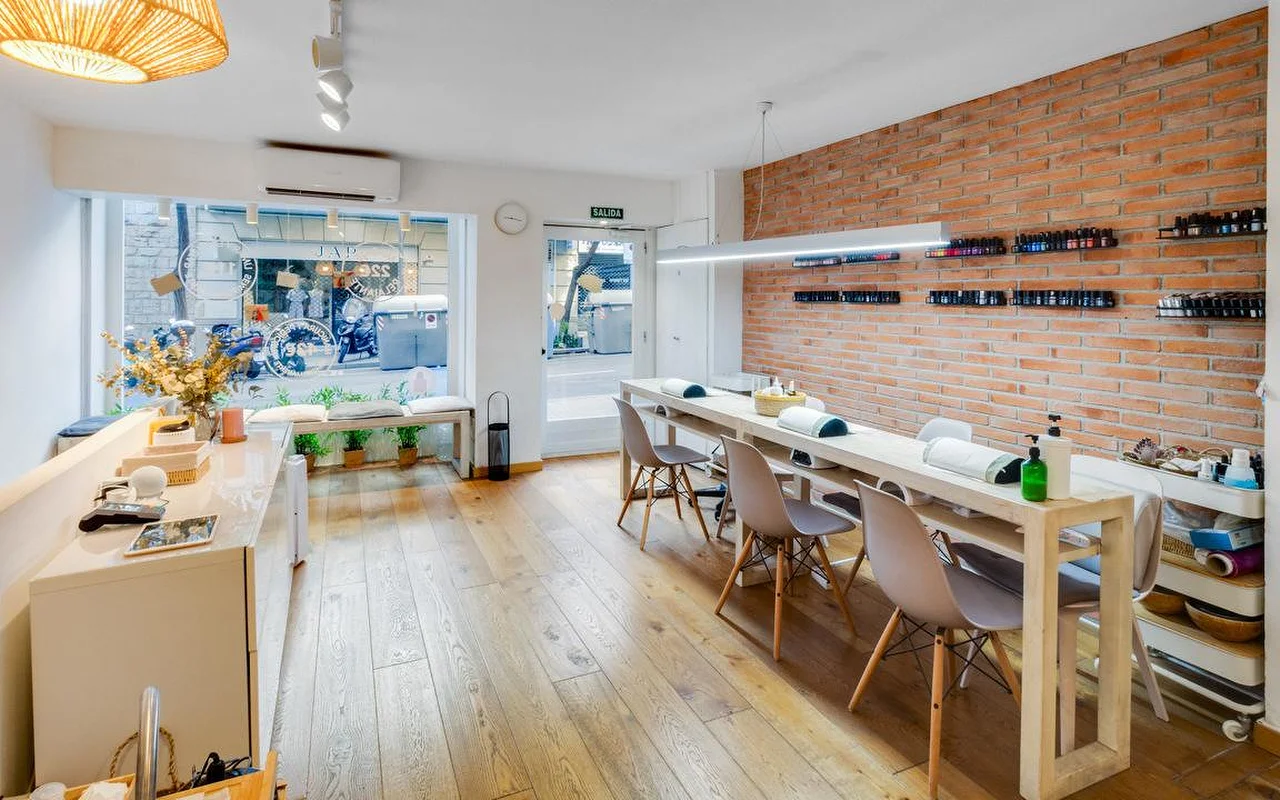 Ein moderner Salon mit rustikalem Akzent: eine lange weie Maniküre-Theke und eine rote Backsteinwand. Groe Fenster blicken auf eine Stadtstrae, und der Holzboden wird von natürlichem Licht durchflutet.