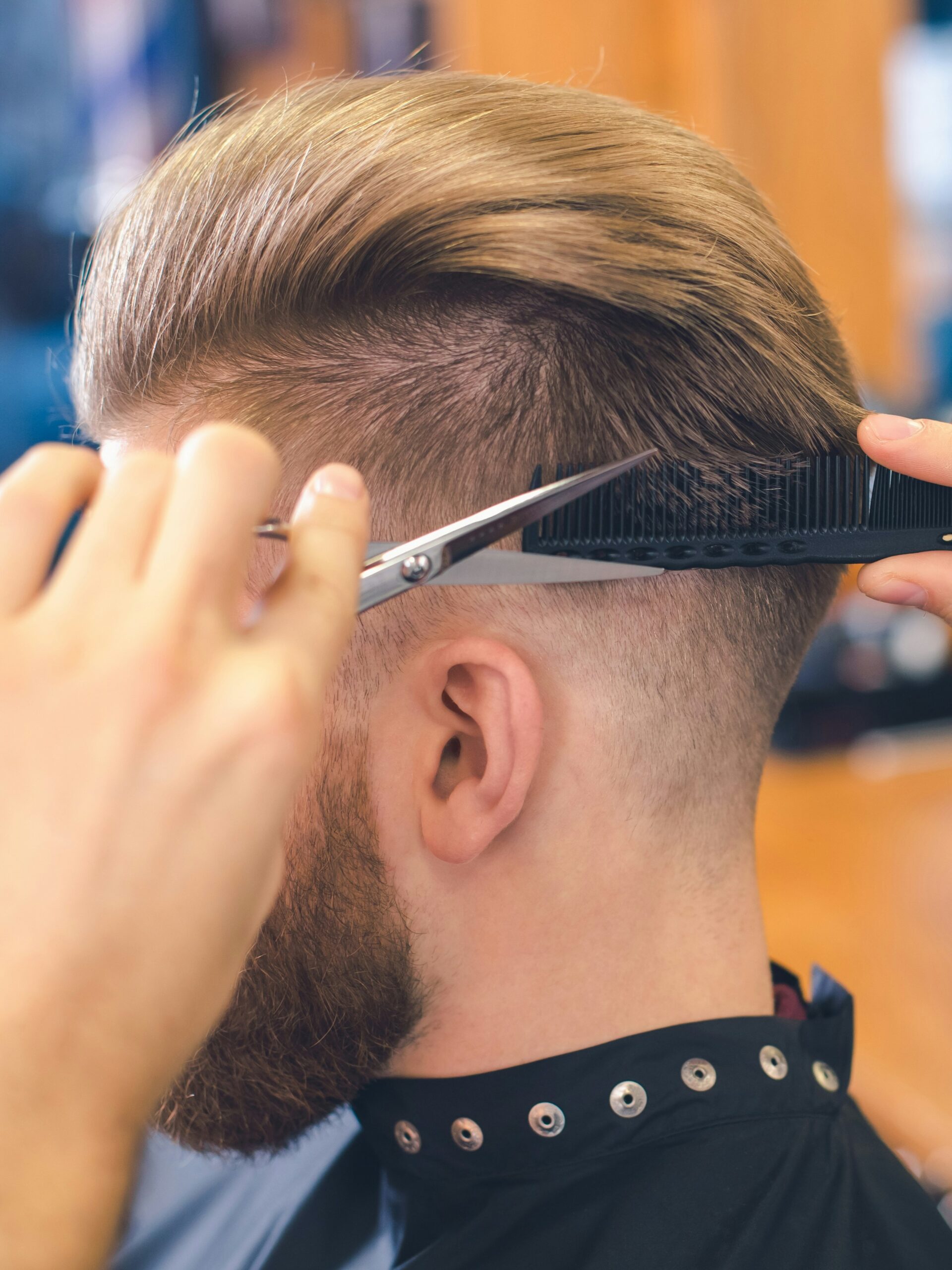 Nahaufnahme eines Barbers, der mit der Schere-über-Kamm-Technik einen Taper Fade am Hinterkopf eines Kunden schneidet
