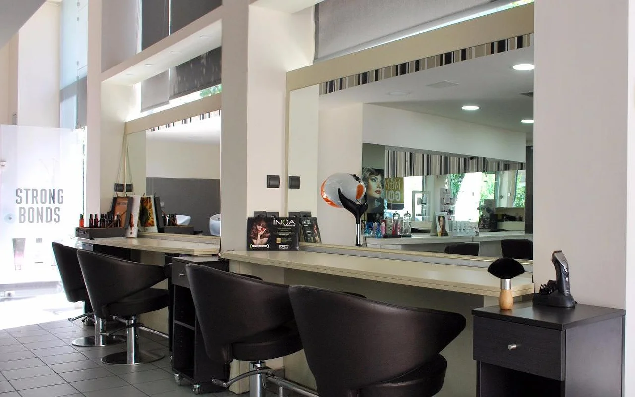 Ein professioneller Friseursalon mit dunklen Leder-Stylingstühlen vor großen Spiegeln, Haarpflegeprodukten entlang der Theke, hohen Decken und natürlichem Licht durch Oberlichter.