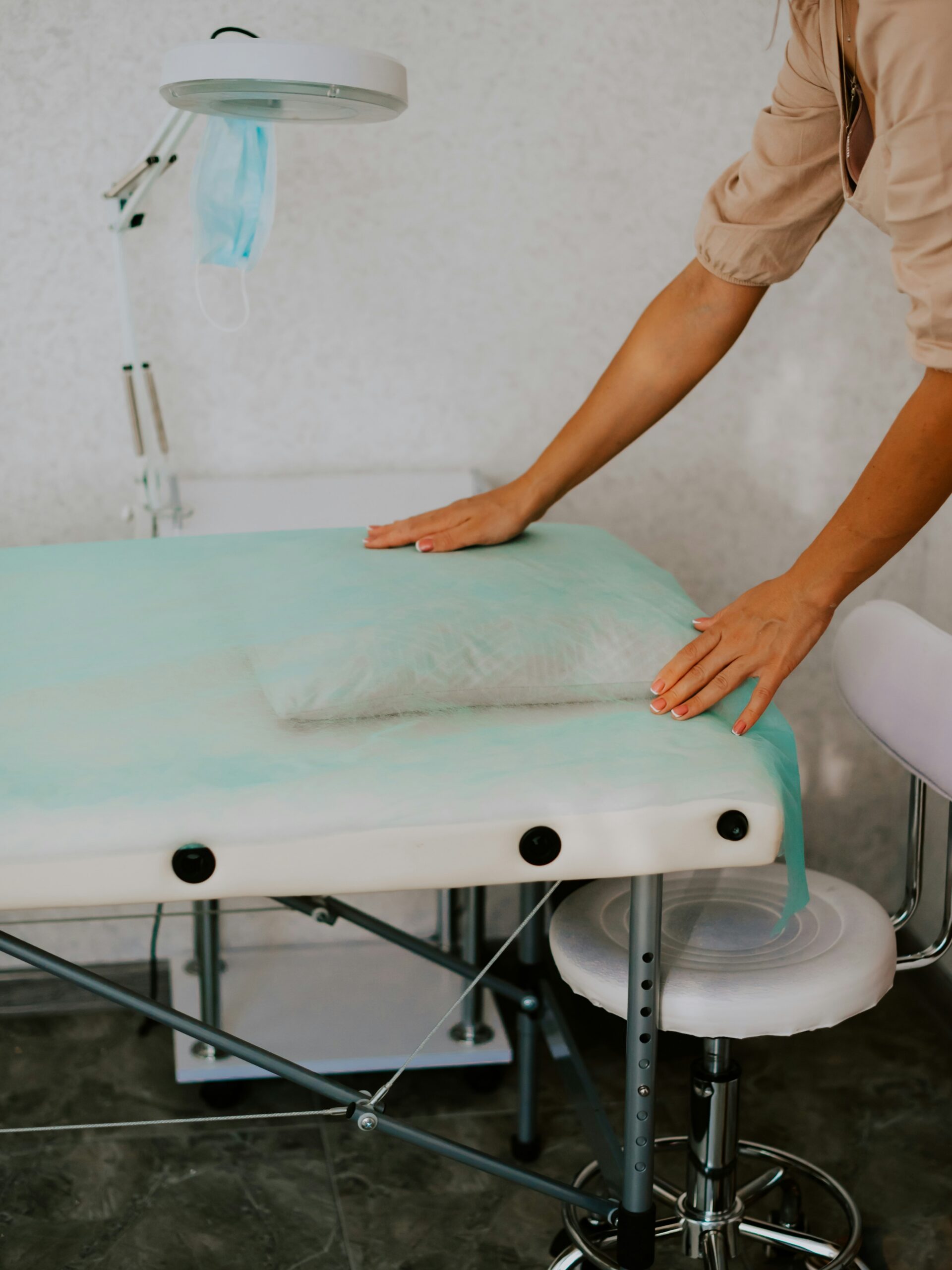 Ein Behandlungsraum im Kosmetikstudio mit einer sauberen, hygienischen Umgebung und einer Fachkraft, die frisches Papier über die Behandlungsliege legt
