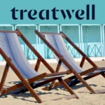 Zwei gestreifte Holzliegestühle im Sand vor pastellblauen Strandkabinen an der Küste der Versilia