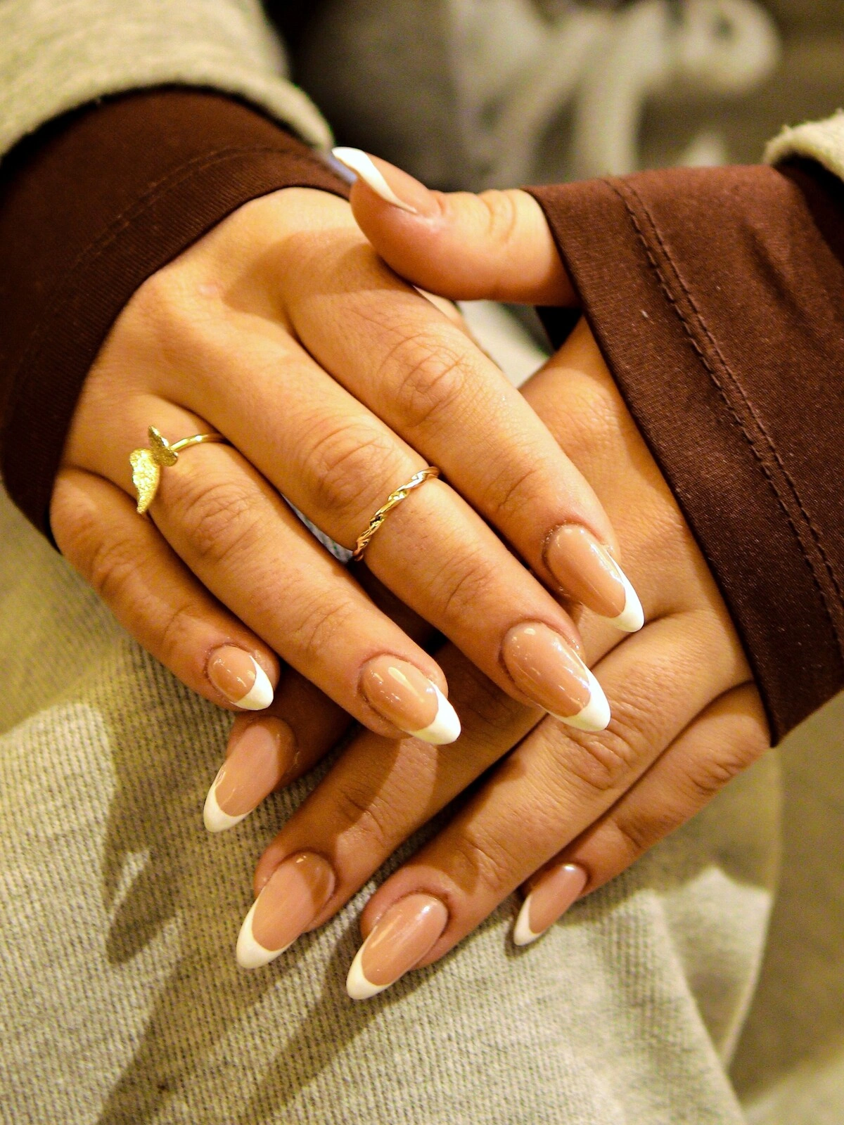 Die Hände einer Frau zeigen eine auffällige French-Tips-Maniküre in einer Kombination aus Beige und Weiß auf langen, mandelförmigen Nägeln