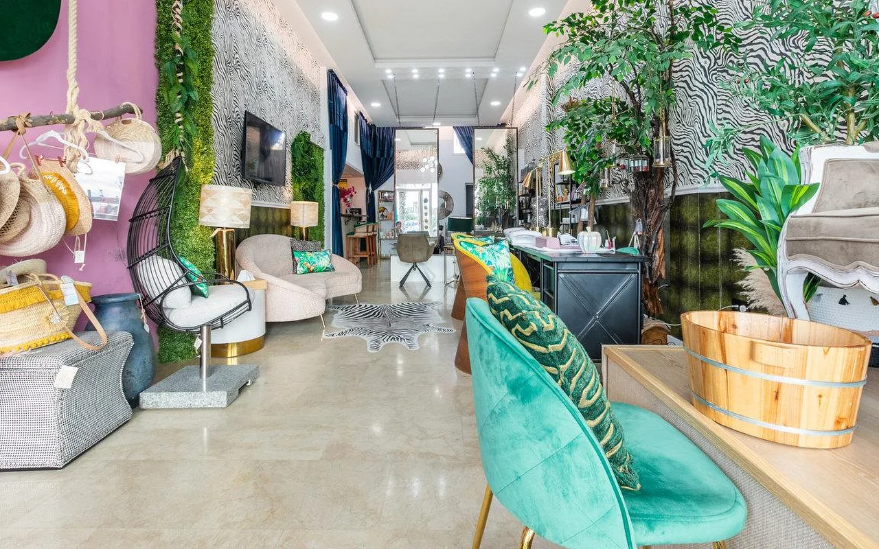 Das Interieur von Brazilian Beauty Marbella, ein heller Salon mit Zebra-Print-Wänden, einer begrünten Pflanzenwand, petrolfarbenen Samtstühlen und einem hölzernen Pediküre-Becken.