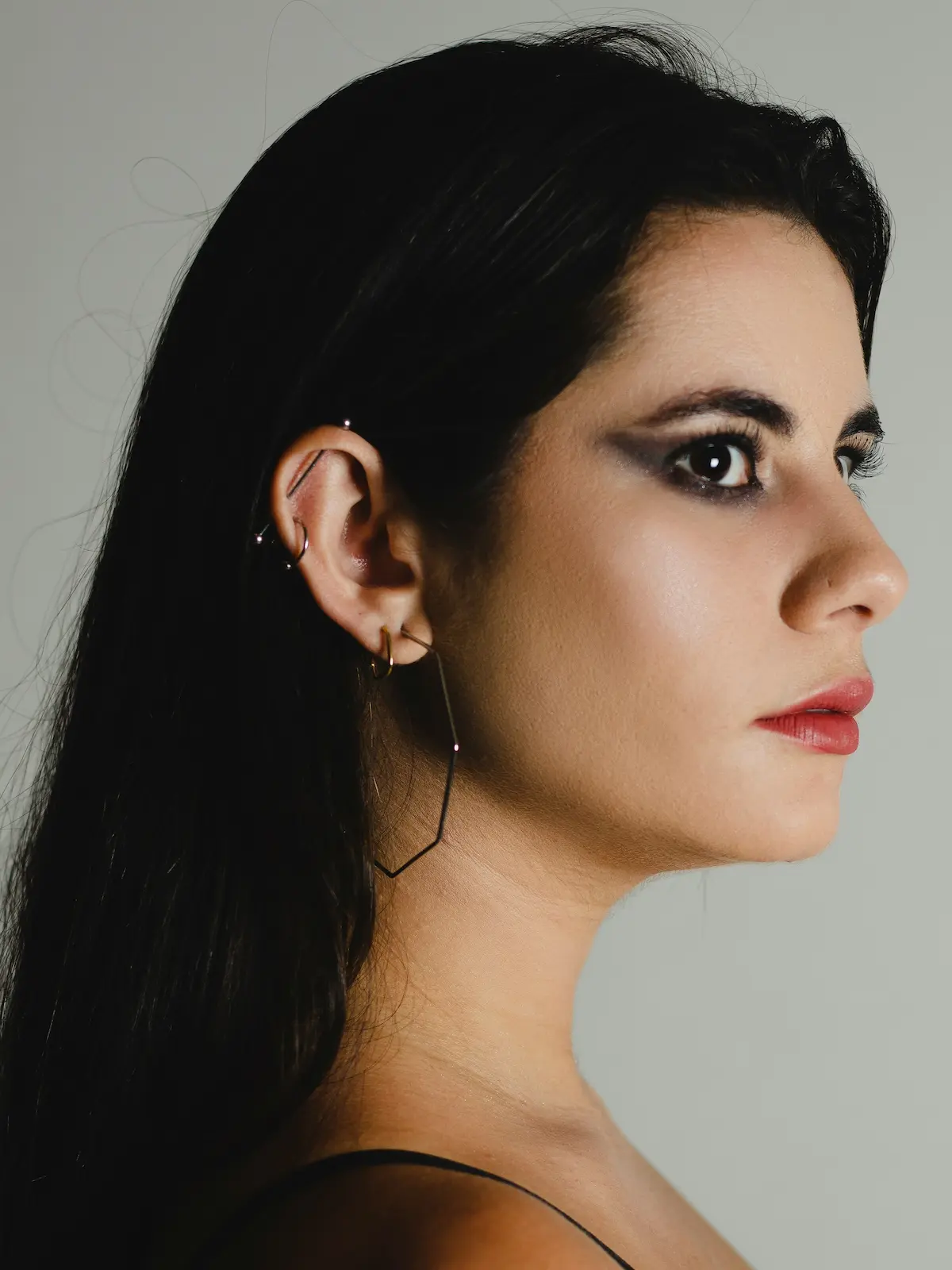 Studioaufnahme einer Frau mit einem Industrial-Barbell sowie Ohrläppchen- und Helix-Piercings