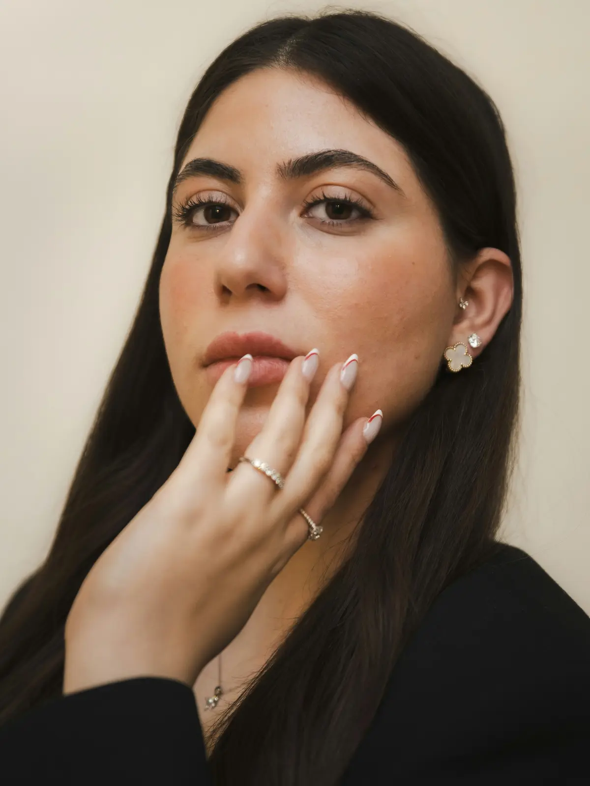 Studioaufnahme einer Frau mit Ohrläppchen- und Tragus-Piercings, die eine manikürte Hand an ihr Gesicht hält