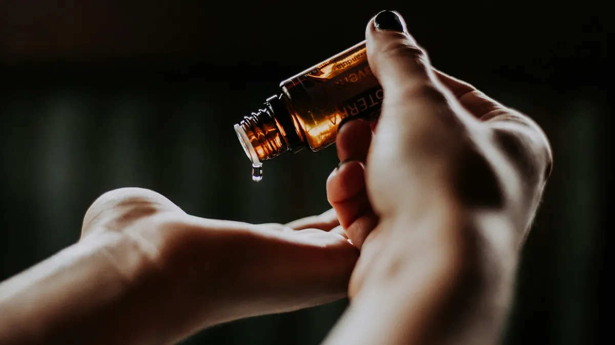 Nahaufnahme der Hände einer Fachkraft, die mit einer Hand Öltropfen aus einer Glasflasche in die Handfläche der anderen gibt