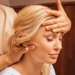 Nahaufnahme einer Frau mit geschlossenen Augen, während eine Fachkraft bei einer indischen Kopfmassage eine Hand auf ihre Stirn legt und mit der anderen ihren Nacken massiert